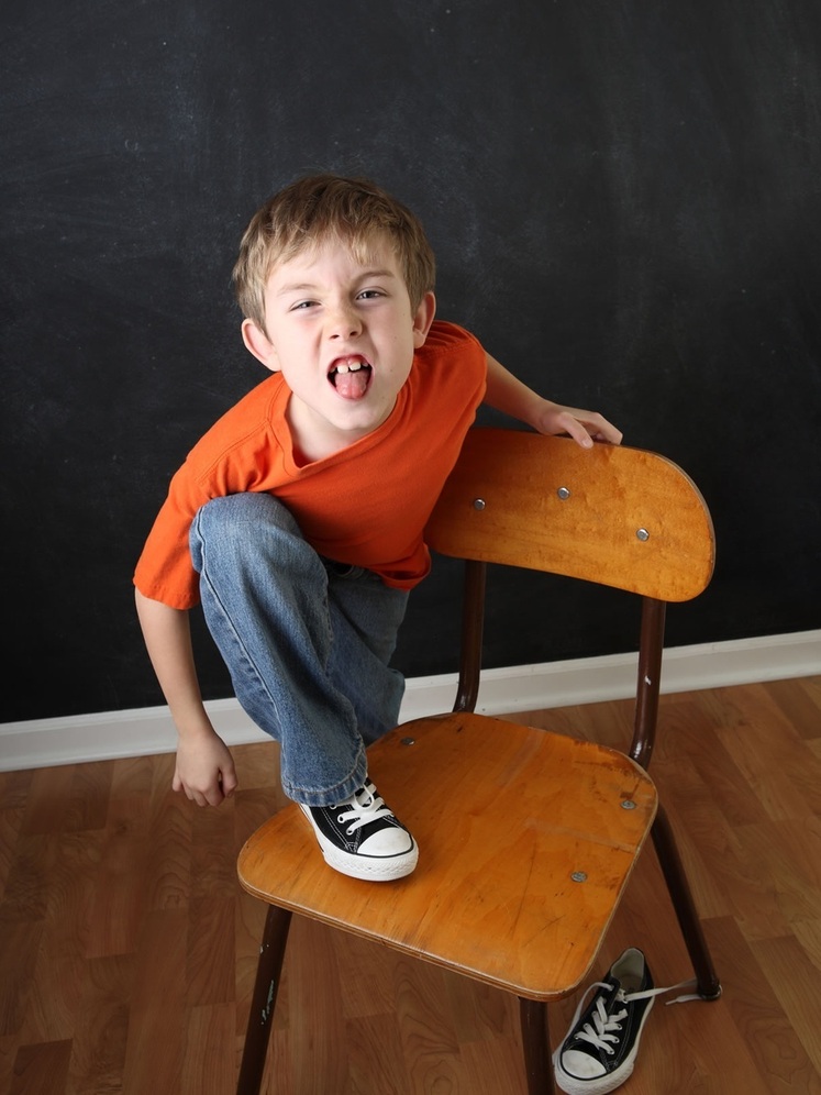 Criança fazendo careta colocando o pé sobre a cadeira - foto: Suzanne Tucker/ShutterStock.com