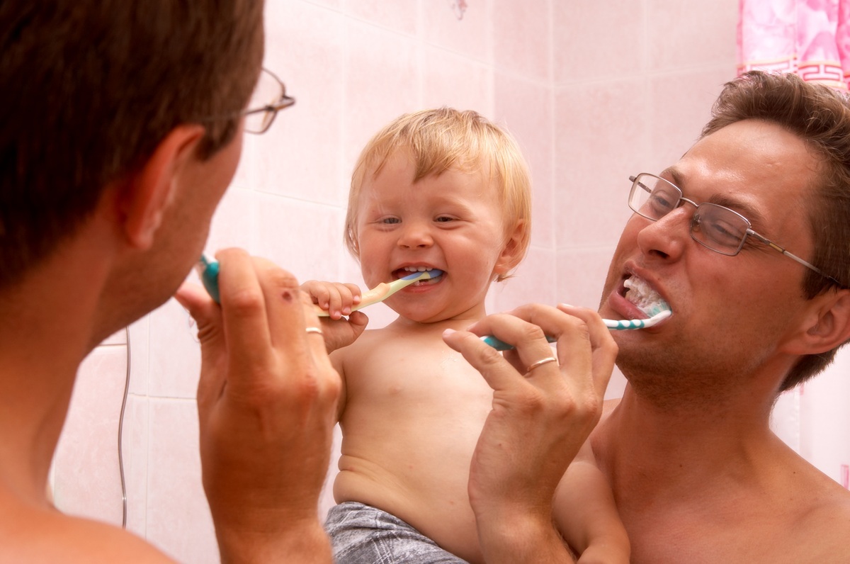 Pai escovando os dentes com o filho no colo - foto: Andrei Vorobiev/ShutterStock.com
