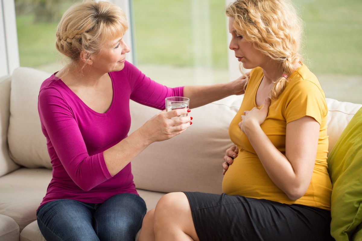 Mãe oferecendo um copo de água para ua filha grávida com falta de ar - foto: Photographee.eu/ShutterStock.com Mãe oferecendo um copo de água para ua filha grávida com falta de ar - foto: Photographee.eu/ShutterStock.com