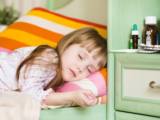 Menina adoentada deitada na cama ao lado de alguns medicamentos - Foto: Ermolaev Alexander/Shutterstock.com