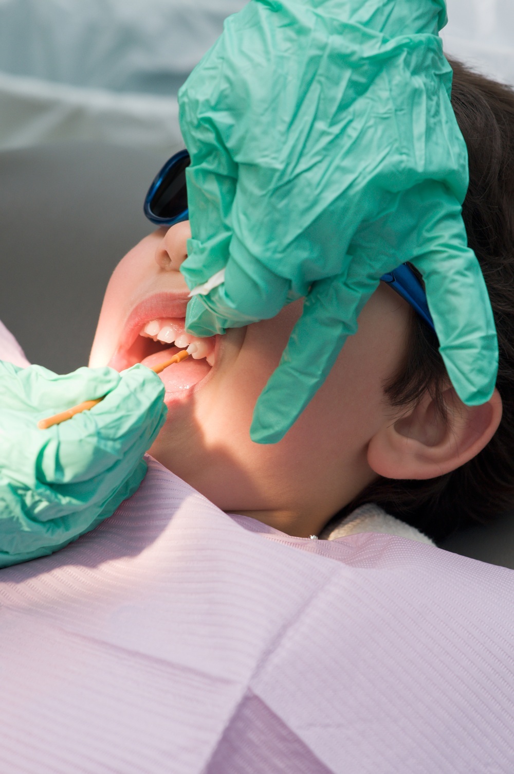 Criança no consultório do dentista recebendo aplicação de flúor nos dentes - foto: nfsphoto/ShutterStock.com