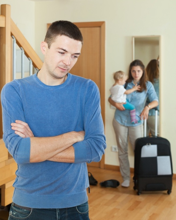 Mãe com o bebê no colo saindo de casa com uma mala enquanto observa o pai da criança - Foto: Iakov Filimonov/Shutterstock.com Mãe com o bebê no colo saindo de casa com uma mala enquanto observa o pai da criança - Foto: Iakov Filimonov/Shutterstock.com